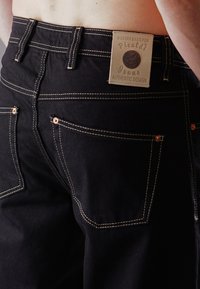 Black denim jeans with contrast stitching, five pockets, and a label showing "Picaldi Jeans Authentic Design." Features copper rivets.