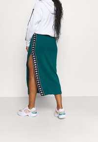 Vihreänsininen midihame sivuhalkiolla, jossa on musta Kappa-logonauha. Yhdistetty valkoiseen huppariin ja valkoisiin urheilullisiin lenkkareihin.