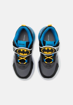Zapatillas infantiles grises y negras con forro azul, cordones amarillos y logo de Batman en las correas ajustables.