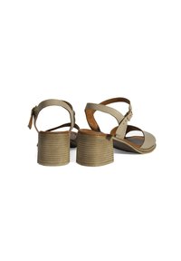 Beige hoge sandaaltjes met gekruiste banden, een gespsluiting rond de enkel en een ribbelige, cilindervormige hak. Soepele textuur en leren materiaal.
