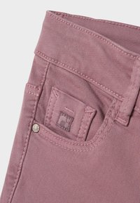 Jeans color rosa con una texture liscia, caratterizzati da una piccola tasca posteriore con dettaglio ricamato e un bottone argentato sulla vita.
