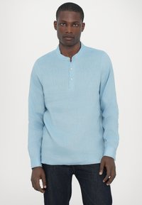 Lyseblå langermet henley-skjorte laget av teksturert stoff, med en knappelukking og rund krage. Brukt med mørke jeans.