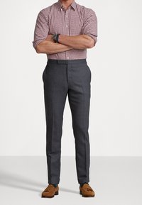 Camicetta a maniche corte a scacchi rossi e bianchi, pantaloni grigi su misura, mocassini in suede marroni. Orologio distintivo al polso, linee pulite e design aderente.