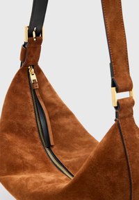 Borsa in suede marrone con forma curva, caratterizzata da una cerniera dorata e dettagli in pelle nera sulle tracolle. Texture liscia e particolari in metallo.