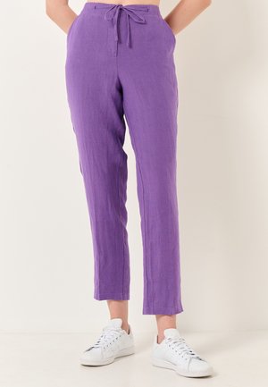 Pantaloni di lino viola con vita regolabile, gambe affusolate e tasche anteriori. Abbinati a sneakers bianche.
