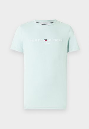 Világos mentazöld pamut póló kerek nyakkal, amelyen fehér "TOMMY HILFIGER EST. 1985" logó és egy kis piros-kék grafikai motívum található.