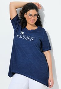 Laivaston sininen ylisuuri T-paita pehmeästä, teksturoidusta kankaasta, jossa on pyöreä pääntie. Vaatteessa on valkoista tekstiä: "tropiikin palmut & AURINGONLASKUT," lyhyet hihat.