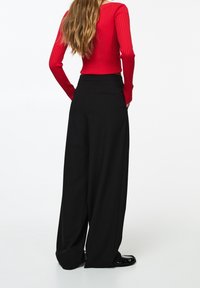 Červený žebrovaný top s dlouhým rukávem spárovaný s vysokými černými širokými kalhotami s zadními kapsami. Hladká textura, dobře střižený střih.