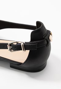 Schwarzer Kunstleder-Schuh mit Knöchelriemen und silberner Schnallendetail, runder Zehenform und flachem Absatz. Glatte Textur mit dezenten Nähten.
