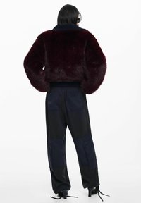 Bordová krátka bunda z umelého kožušiny so žebrovaným námorníckym golierom, v kombinácii s tmavými cargo nohavicami s nášivkovými vreckami a voľným strihom.