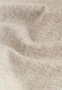Tissu tissé beige avec un motif texturé en forme de grille. Texture douce avec des variations subtiles de teinte et de densité.
