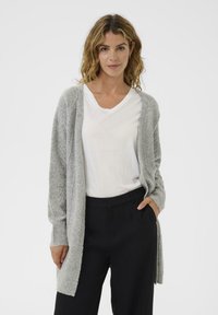 Ljust grå stickad cardigan med avslappnad passform, featuring en texturerad mönster, öppen front och ribbade ärmar, tillsammans med en vit t-shirt och svarta byxor.