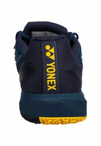 Navy athletic shoe with textured fabric upper, yellow "YONEX" branding, and a visible patterned rubber outsole in contrasting yellow and black.
