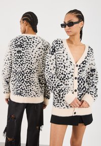 Crop cardigan in a cream color with a black abstract pattern. Features a deep V-neck, button front closure, and ribbed cuffs and hem.