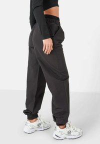 Pantalones de chándal negros con un corte holgado, cintura elástica, bolsillos laterales y puños gathered, combinados con zapatillas deportivas blancas.