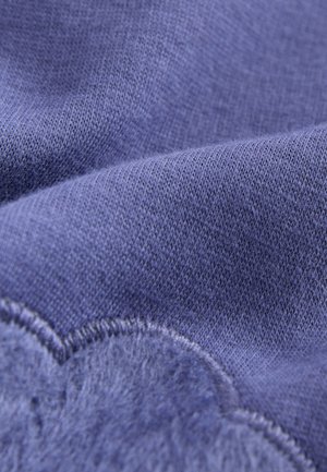 Textura de tela morada con un suave y difuso adorno en forma de nube y un detalle de costura en contraste. Superficie lisa y ligeramente reflectante.