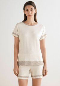 Conjunto de ropa de estar en color crema que incluye una blusa de manga corta y pantalones cortos, acentuado con delicados bordes de encaje en las mangas y el dobladillo.