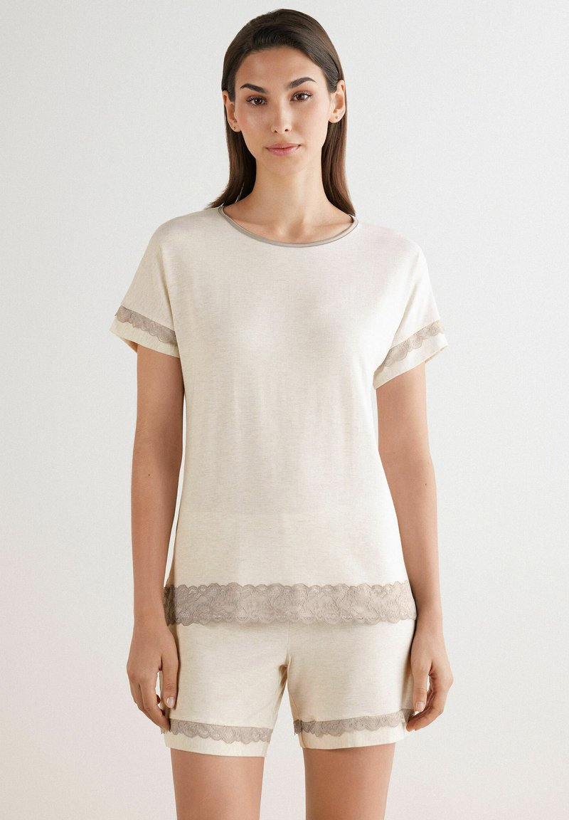 Conjunto de ropa de estar en color crema que incluye una blusa de manga corta y pantalones cortos, acentuado con delicados bordes de encaje en las mangas y el dobladillo.
