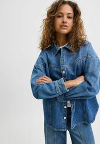 Denim jacket featuring a relaxed fit, light blue wash, button front, and large pockets. Textured fabric with slight fading.