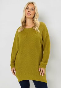 Olive vihreä neulepaita, jossa on väljä malli, pitkät hiijat, röyhelökäärme ja pyöreä kaula-aukko, jossa on teksturoitu kuvio koko vaatteessa.