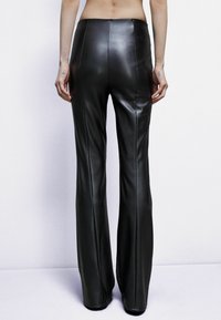 Pantaloni neri in pelle a zampa d'elefante con una texture liscia, dotati di cuciture verticali e una vita alta, visti da dietro su uno sfondo neutro.