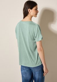 T-shirt verde chiaro a maniche corte con vestibilità rilassata, orli arrotolati e orlo leggermente curvo, realizzato in un tessuto morbido e testurizzato.