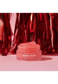 Rosa, gjennomsiktig leppebalsam i et klart, rundt glass med skrulokk. Etiketten viser "NCLA Beauty Balm Babe," 10 mL. Skinnende rød bakgrunn.