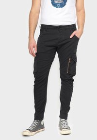 Zwarte cargobroek met ritszakken, gemaakt van katoenen stof. Tapered fit met zijzakken, gecombineerd met grijze hoge sneakers.