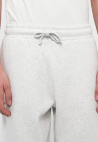Pantalones de chándal gris claro hechos de un tejido suave y texturizado, con un cinturilla elástica y un cordón, y bolsillos laterales para mayor funcionalidad.