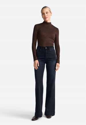 Top brown a maniche lunghe con collo alto abbinato a jeans in denim scuro a vita alta e a zampa. Texture liscia, design aderente, dettagli minimal.