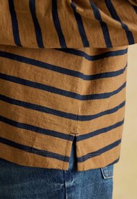 Pruun ja tumesinine triibuline lühikeste varrukatega särk, millel on külgmine lõhik, kootud tekstuur ja ääred on korralikult lõpetatud, koos denimpäevade siniste teksadega.