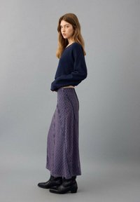 Navy sweater with long sleeves, paired with a flowing purple skirt featuring circular patterns. Black ankle boots complete the outfit.