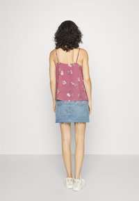 Wiskozowa bluzka na cienkich ramiączkach w kolorze mauve z kwiatowym nadrukiem, w zestawieniu z jasnoniebieską spódnicą dżinsową z postrzępionym dołem, noszona z białymi sneakersami.