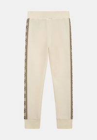 Pantalons de jogging couleur crème avec une texture douce, présentant des rayures latérales à motif logo et des poignets et une taille élastiqués.