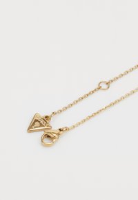 Gold-tone necklace featuring a triangular pendant with "GUESS?" engraving, linked by a fine chain, and a lobster clasp closure.