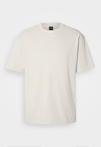 T-shirt écru à manches courtes avec col rond et une petite étiquette noire à l'intérieur du col arrière affichant le nom de la marque.