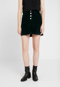 Dark green corduroy skirt with a fitted waist, five silver snap buttons at the front, and a slight A-line shape. Worn with black ankle boots.