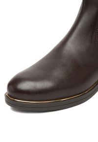 Bota de cuero marrón con punta redondeada, textura suave y un sutil detalle dorado a lo largo de la suela. Diseño elegante con perfil bajo.