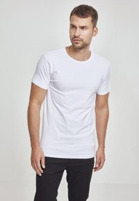 Tricou alb din bumbac cu guler rotund și mâneci scurte, design ajustat, asortat cu pantaloni negri, stil minimalist, textură simplă.