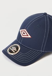 Ναυτικό μπλε καπέλο βάσης με λευκές ραφές και κεντημένο λογότυπο. Διαθέτει κυρτό γείσο και ρυθμιζόμενο λουρί με ετικέτα.