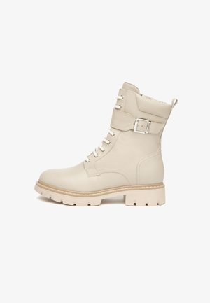 Bottine en cuir beige avec semelle robuste, lacets sur le devant et sangle ajustable avec boucle métallique. Texture lisse, design pratique.