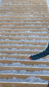 Lesena stopnišča, pokrita z zaplatami snega, ob desni strani oseba v modri jakni z iztegnjeno roko.