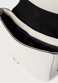 Hvid læderhåndtaske med en tekstureret overflade. Åben top afslører en sort indmad med en lynlåslomme og et mærke, som har kontrastsyninger.