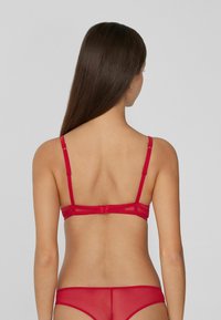 Rotes Lingerie-Set bestehend aus einem BH aus transparenter Stoff mit verstellbaren Trägern und einem Haken- und Ösenverschluss, begleitet von passenden Panties.