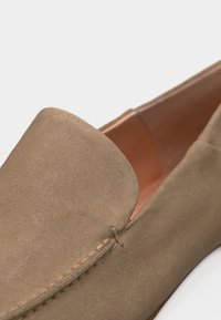 Κοντινό πλάνο μπεζ μοκασίνι από σουέντ που δείχνει λεπτομερές ράψιμο κατά μήκος της άνω ακμής και λείο δερμάτινο εσωτερικό.