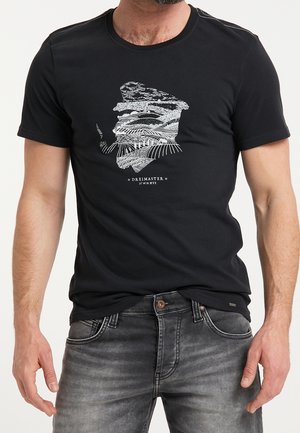 Homme portant un t-shirt noir avec un graphique blanc représentant une silhouette barbu fumant une pipe, assorti à un jean noir délavé.