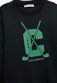 Czarna bluza wykonana z mieszanki bawełny. Posiada zieloną grafikę z literą "C," rokiem "1984" oraz skrzyżowanymi kijami hokejowymi. Ribbed neckline.