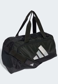 Svart duffelbag laget av teksturert nylonmateriale, med to topphåndtak, en justerbar skulderrem og en stor sølvfarget grafisk logo.