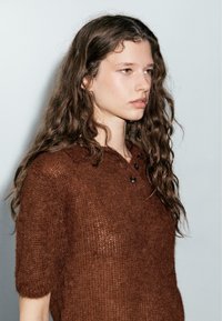 Bruine gebreide polo met korte mouwen en een losse pasvorm, met een gestructureerd oppervlak, drie knopen bij de kraag en een zachte, fuzzy afwerking.