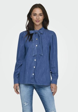 Blusa in denim, azzurro chiaro, con colletto a fiocco, maniche lunghe e chiusura con bottoni. Caratterizzata da una vestibilità rilassata e una texture delicata.
